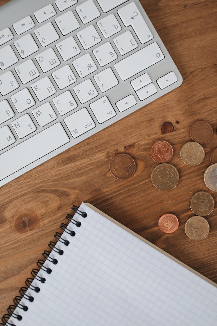 Organized workspace showing a keyboard, coins, and notebook on a wooden table.